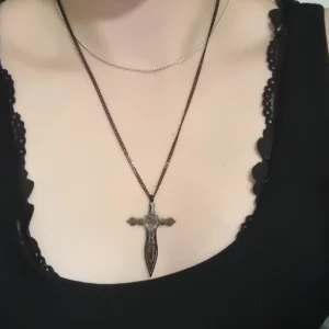 Svart svärd/kors halsband  - Ett vackert, halsband med en ros i mitten. Köpt på en piercing studio för något år sedan men har inte använts då jag mestadels har samma halsband. Bra kvalité, kedja ingår självklart. 