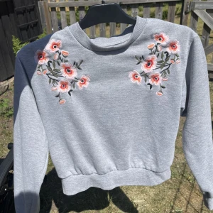 Sweatshirt - ⚠️Smutsig spegel⚠️ En fin grå sweatshirt med blommor vid axlarna. Den har använts en del men inga tecken på användning finns.  Referens: jag bär vanligtvis M.
