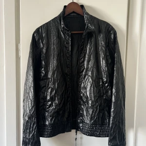 ”Läder”jacka, strl 46 - Emporio Armani jacka, strl 46 Helt ny med tags  Exotisk lädereffekt på polyester Nypris 8000, mitt pris 3500kr  Mått:  Armhåla till armhåla: 46 cm Axelbredd: 43 cm Ärmlängd: 65 cm Total längd: 67 cm  Har mycket tidigare säljarrecensioner från andra sidor 