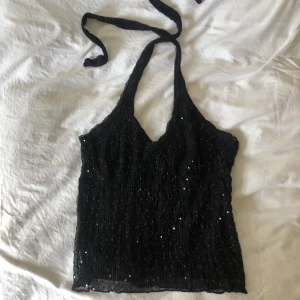 halternecktop paljetter strl XL - En halternecktop i stretchigt material, med svart paljetter. I gott skick utan tecken på användning. Midjemått på ungefär 80cm (strl M) men kan enkelt anpassa större mått. Köparen står för frakt. Dma gärna vid frågor eller funderingar!