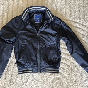 Ridjacka  - En fin, marinblå, varm ridjacka i storlek XS. Går till midjan och är i modellen bomberjacka.  Material: polyester Dragkedja på fickor Finns innerficka Funkar bra till höst och vinter när man rider. Jackan är använd några år därför det bra priset!