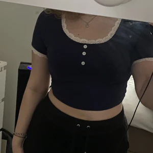 Marinblå topp med spets - Jättegullig oanvänd marinblå topp med vit fin spets och knappar framtill. Jätteskönt och Stretchigt material t våren o sommaren. Strl S men funkar t M, 60kr+frakt 