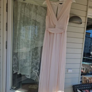 Puderrosa festklänning  - Puderrosa festklänning säljes. Öppen i övre ryggen. Nedre ryggen har dold dragkedja.  Har ett avtagbart band i midjan.   Inköpt ca 2015. Använd en gång. Som ny.