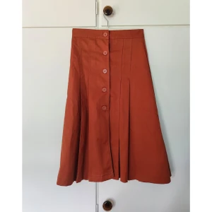 Härlig utsvängd kjol med knappar - Brons brun kjol i härligt tyg, ej använd. Okänt märke!  Finns en fläck på höger höft som knappt syns (se bild) 