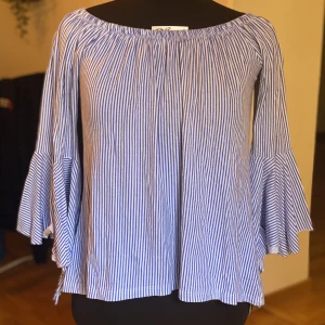 Blå/vit randig blus - Blå/vit randig tröja/blus med volang till ärmarna. Går att ha off-shoulder men även som vanligt. Finns inget märke eller satt storlek men passar M. Vitt lite tjockare innetyg som gör det perfekt till hösten! 