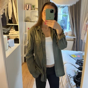 Skjortjacka - Militärgrön skjorta från Gina Tricot med ett coolt märke på höger arm. Skjortan går superbra att använda som jacka!! Storleken är 36 men passar mig som vanligtvis bär 34❤️Skicket är som nytt då jag aldrig använt den. Hör av er vid frågor eller fler bilder🤘🏻