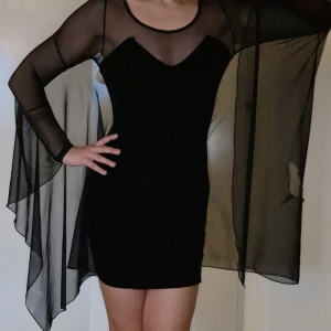 Unik goth batwing klänning i sammet och mesh storlek 36 - Unik vintage klänning i "sammets"tyg & långa mesh-ärmar. Otroligt vacker & i superskick förutom ett hål i meshen, syns på foto 2. Kort figurnära modell. Passa på innan jag ångrar mig 😅 Använd köp-knappen 💖💖💖