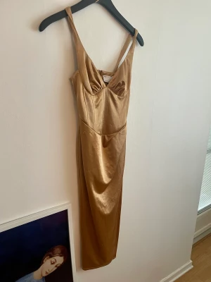 Guldfärgad festklänning - Jättefin guldig midiklänning i satin med rysch och korsettdetalj från Asos. Lite nopprig som syns på sista bilden. Använd en kväll. Nypris var 640 kr. Perfekt på fest!! 