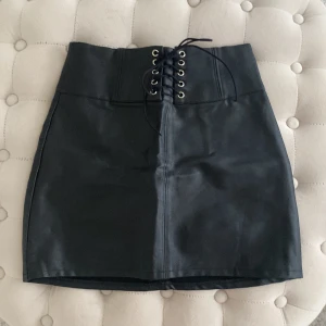 Faux skinnkjol - Kort kjol i skinnimitation, dragkedja bak. Använd fåtal gånger. Snörningen fram är detalj , går ej justera för att minska eller förstora midjan