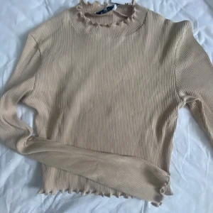 Topp  - Långärmad lite croppad topp som är helt oanvänd. Lite utsvängd i armarna och volanger i krage och armar. 