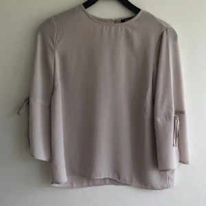 Beige blus  - Säljer denna söta toppen med volanger och knyten på ärmarna. Skönt, svalt material. Knappt använd så väldigt fint skick. Rensar bland kläderna så kolla gärna mina andra annonser också 🤗