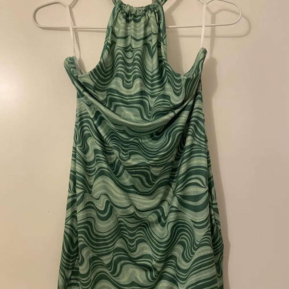 En grön mönstrad klänning som har ett tunt material med en låg öppen rygg och knyte vid halsen. Oanvänd och köparen står för frakten . Klänningar.
