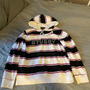 Stüssy hoodie med ränder i vit, svart och lila/röd. Bra skick, köpt second hand därav en liten fläck där bak men inget som stör. Snabb leverans, fler bilder finns 