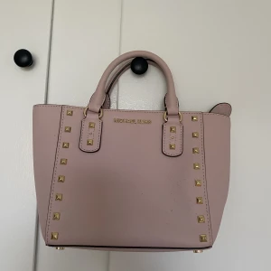 Michael Kors handväska - En mindre ljusrosa handväska från Michael Kors. Sparsamt använd och i mycket bra skick, finnsäven ett band att ha över axeln