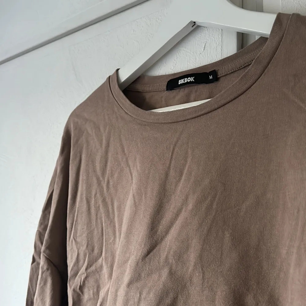 Ljusbrun/begie croppad långärmad tröja som har en öppning i ryggslutet med knyte. Köpt från bikbok och använd enstaka gånger.  Storlek M. T-shirts.