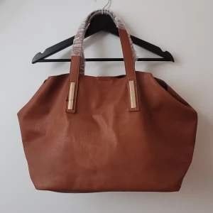 NY stor väska brun fejk läder - Stor väska brun faux leather gulddetaljer med insats som kan tas ur med tryckknappar. Aldrig använd. Nypris 399 kr. Katt har funnits i hemmet 🐱 Pris kan diskuteras vid snabb affär, skickas eller möter upp/hämtas i Gbg. PM för mer detaljer/frågor/bud!