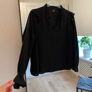 Svart blus från Gina Tricot med volanger vid ärmslut och axlar.  Använd men utan anmärkningar och har mycket kvar att ge 🧡  Storlek 34 