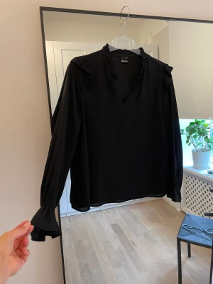 Svart blus - Svart blus från Gina Tricot med volanger vid ärmslut och axlar.  Använd men utan anmärkningar och har mycket kvar att ge 🧡  Storlek 34 