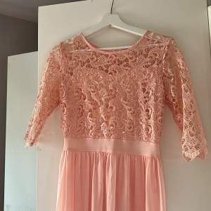 Light peach/ ljus rosa lång klänning. Den har spetsupptill och sedan en tunn lång kjol. 