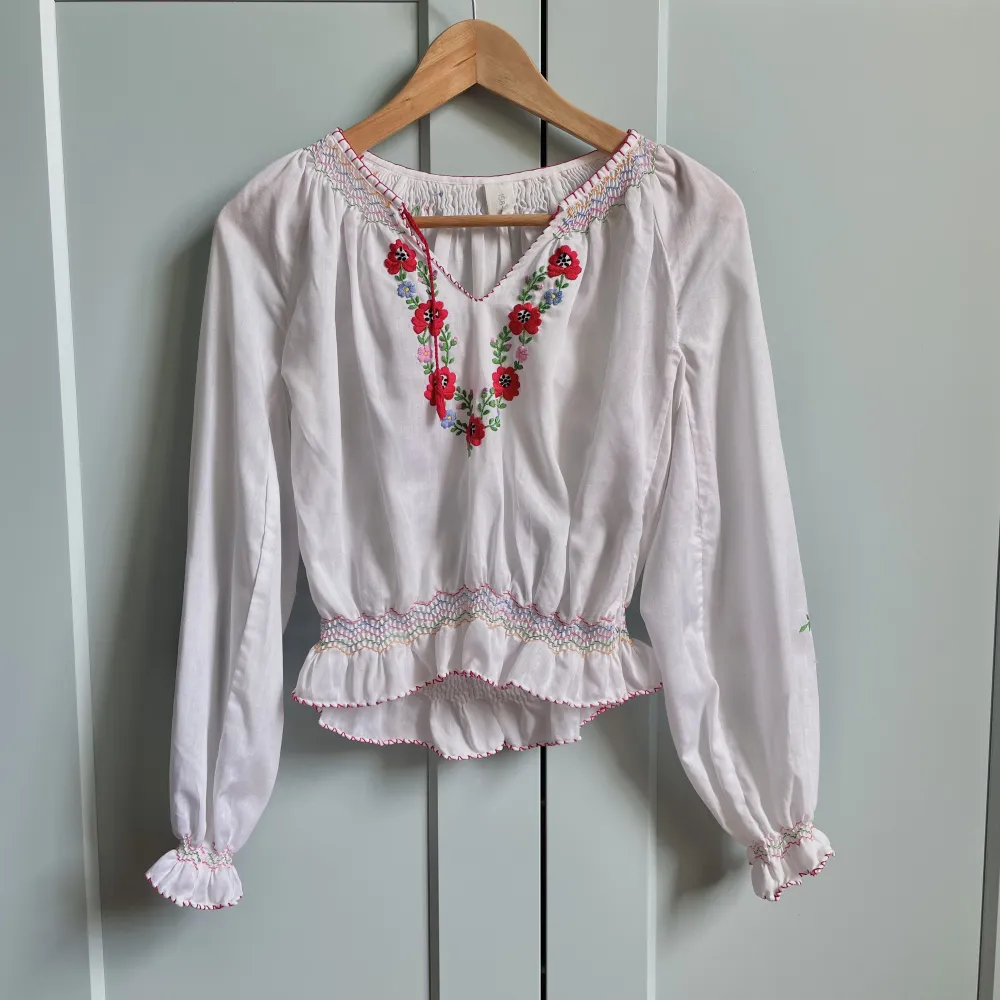 Vintage Cotton Blouse with Embroidered Flowers and Colored Stitching Details. Frontal Red Tie & Feminine Silhouette.  Design could be Hungarian 48 CM/ 18.9 IN Length 58 CM/ 22.8 IN Sleeve 40 CM/ 15.7 IN Shoulders 70 CM/ 27.6 IN Chest 56 CM/ 22 IN Waist. Toppar.