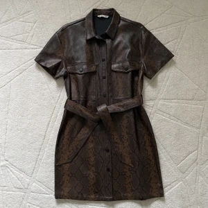 Brun Ormskinnsmönstrad Klänning • Dress  - Kort skjortklänning i ormskinnsmönster med knytning i midjan och knappar. Aldrig använd/ Nyskick! 🤎