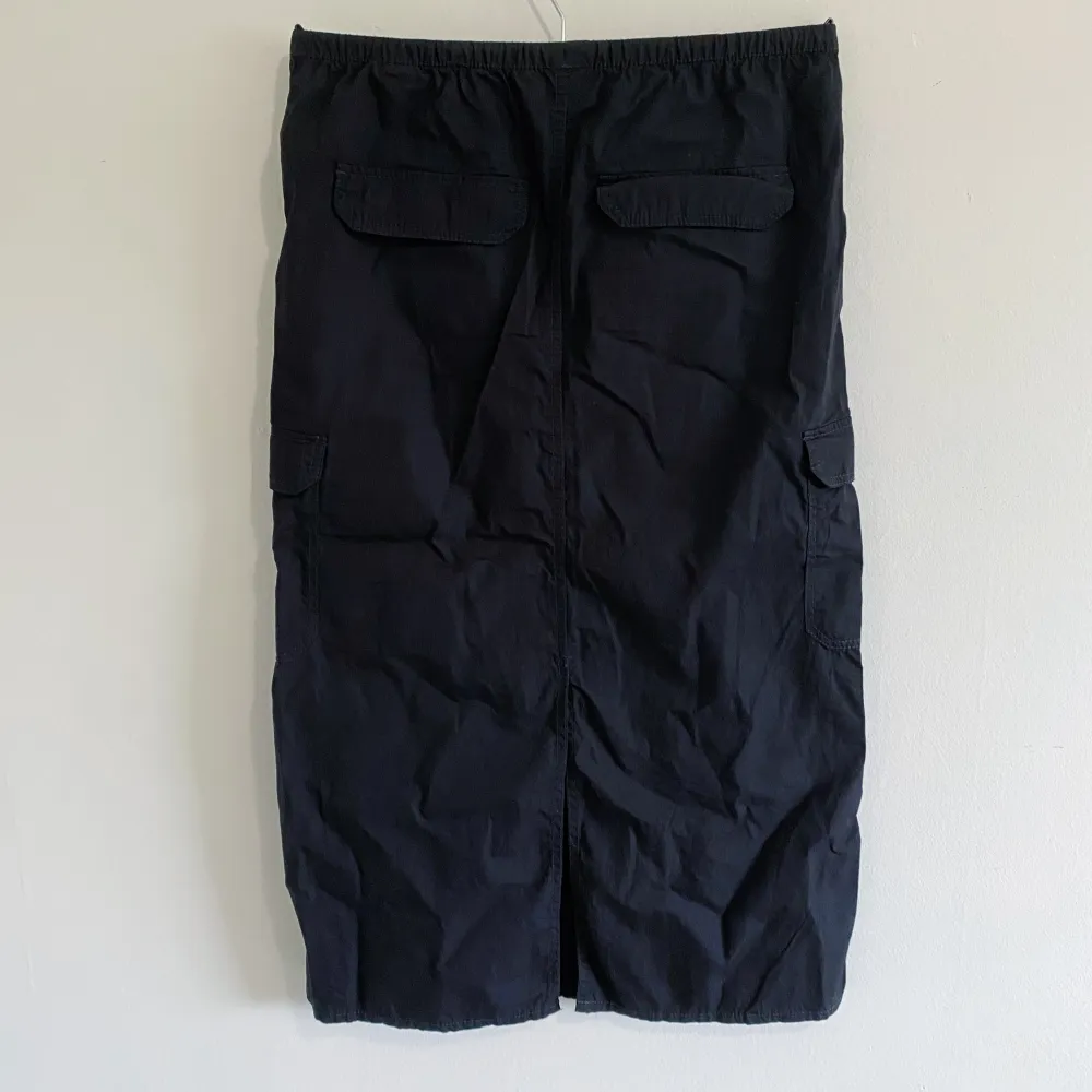 Oanvänd svart cargokjol från H&M. Dragsko i midjan men många fickor, slitt i bak. Längd: 28 cm.. Kjolar.