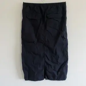 Oanvänd svart cargokjol från H&M. Dragsko i midjan men många fickor, slitt i bak. Längd: 28 cm.
