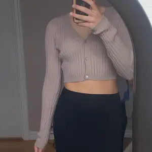 Det är en kort, långärmad tröja från H&M. Den är stretchig med knappar. Färgen är en blandning av beige, lila/rosa och grå.  Storlek S 