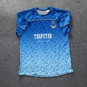 Oanvänd Trapstar irongate Jersey i färgen blå. Tröjan är strl M och är riktigt skön och perfekt för fotboll eller bara för ha bäst stil bland vännerna