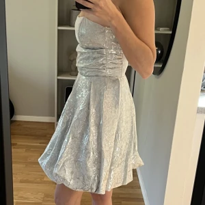 Festklänning  - Vacker cocktailklänning i silver, armlös med dragkedja baktill. Använd 3 gånger, strl XS, jag köpte den för 950kr.