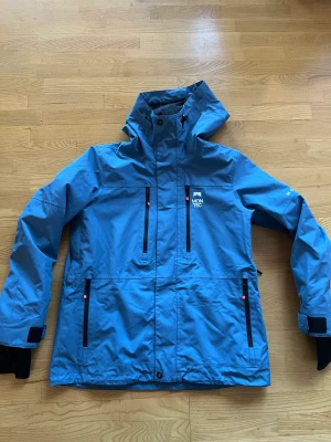 Skidjacka  - Skaljacka för skidåkning. Använd två veckor i fjällen. Nypris 2000kr.  Finns fack för liftkort, även en innerficka.  Finns snö lås.  Kan öppna armhålorna för luftinsläpp.