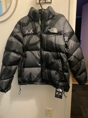 The north face x Kaws retro - Säljs åt mamman då den inta hamnade riktigt i hennes smak. Passar också men med stl M och  tjejer med stl L. Svårt att få tag på. 