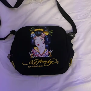 Väska - Säljer min ed hardy väska då jag inte använder den längre. Den har en smink fläck på insidan som du kan se på andra bilden men ska göra mitt bästa på att ta bort den innan köp!