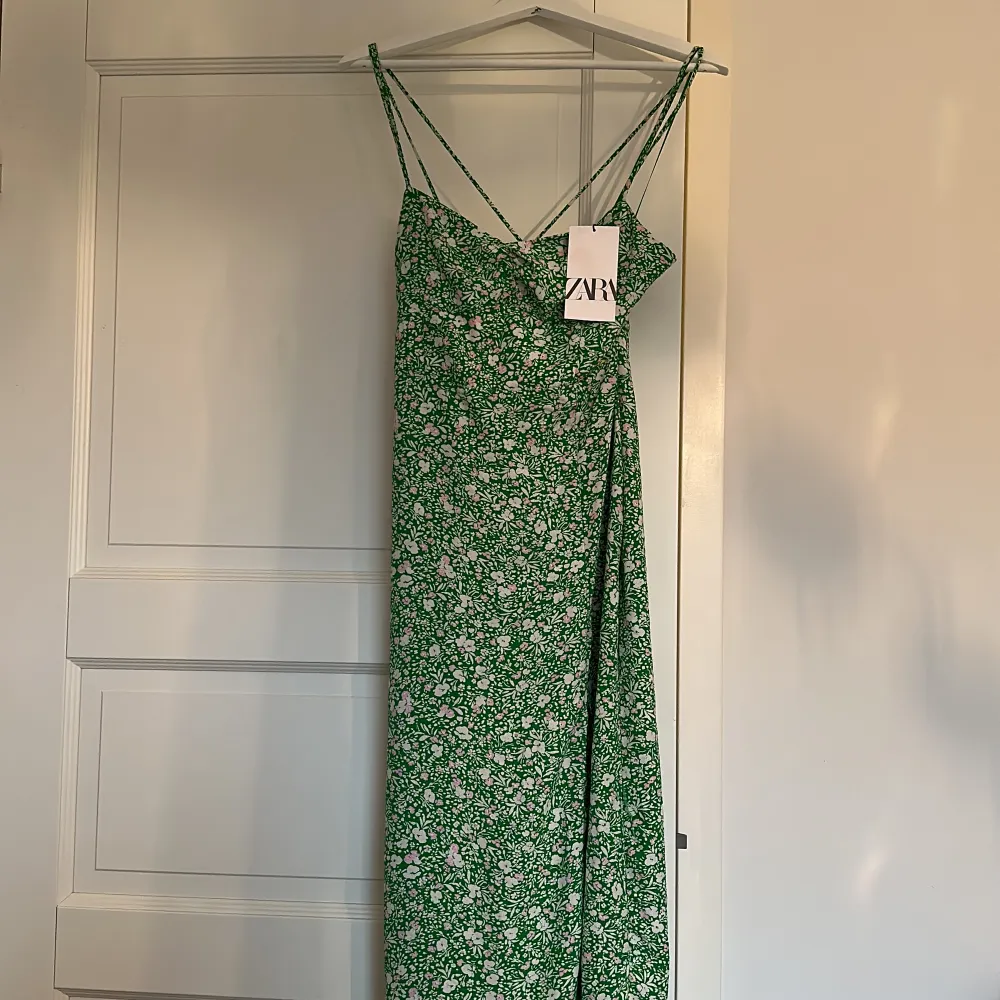 Grön blommig klänning från Zara. Endast provad så prislapp kvar. Nypris 399:- Lite sömskada vid slitsen framtill (se bild). Klänningar.
