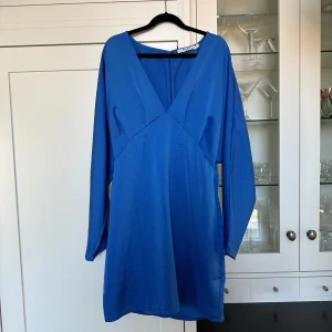 Blå batwing klänning NA-KD, storlek 36 - Långärmad klänning från NA-KD med batwing-ärmar och gömd dragkedja i ryggen. V-ringad. Använd endast en gång😊modellen på bilden är 173 cm. Nypris 450kr. 
