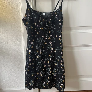 Klänning  - Svart klänning med blommor från hm. Knut framtill. Kort.