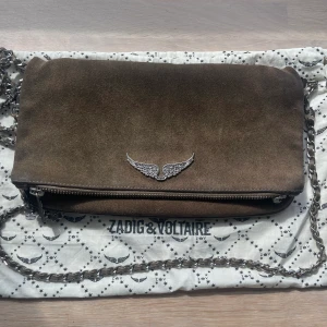Zadig et Voltaire väska - Superfin Zadig väska i brun mocka. Lite tecken på användning finns men i väldigt fint skick med båda remmarna kvar och dustbag. Handtaget på en av dragkedjornas ändar har lossnat men påverkar inte funktionen💖💖 Nypris 4500
