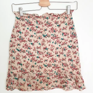 Blommig Kjol - Comfy Mini Skirt with frills in a pink/green floral pattern  Size: s, but it is extremely stretchy so it would fit an m without doubt  Used although in great condition.