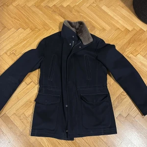Loro Piana / Rose & Born jacka i mörkblå, avtagbar pälskrage - Riktigt snygg vinterjacka i Loro Piana-tyg gjord i Italien av Rose & Born, avtagbar pälskrage, tidlös och  verkligt bra kvalitet - sparsamt använd. Nypris ca 16 000 kr.