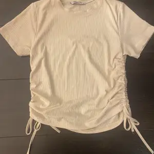 Super snygg beige T-shirt med snören på sidorna som är skjusterbara beroende på hur kort du vill att tröjan ska va. Köparen står för frakt 50kr+frakt☺️