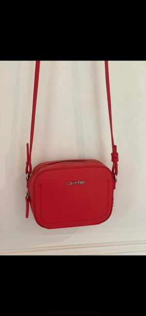 Axelrems väska från Calvin Klein - Liten axelremsväska i cerisefärg med inslag av röd i färgen.   I mycket gott skick!