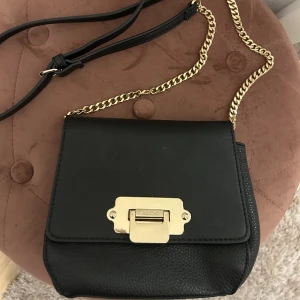 Crossbody väska från Aldo  - En svart crossbody väska från Aldo. Guldiga detaljer, immitations läder och justerbart band. 