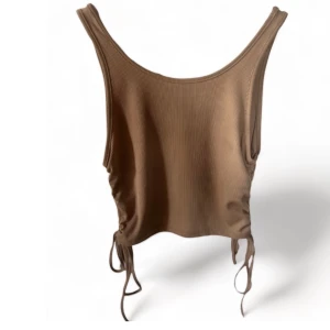 RIBBAT LINNE - Säljer ett linne i färgen beige med två snörningar på sidan som man kan välja att dra åt mer eller ha de mer slappt. Storlek: S  Det finns inga defekter.  Kund står för frakt! 