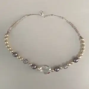 Halsband gjort av både stora och små pärlor i färgerna lila, grå , transparant, vit och ljusrosa.  Gjort av tunn silvrig ståltråd och är handgjort. Köpare står för frakt. 