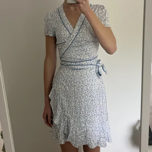 blommig vit klänning  - vit klänning med blåa blommor på från bikbok i omlott modell som ger fin figur. strlk S och inte använd så mkt 🤍 