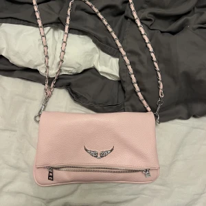 Rosa Zadig väska - Jag säljer min jätte fina men fejk zadigväska då den aldrig kommer till användning. Väskan är helt ny och använd några få gånger. Materialet är väldigt bra för att inte vara äkta och väskan känns överlag som en ordentlig väska med bra dragkedjor osv.