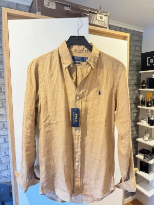 Linneskjorta från Polo Ralph Lauren - Snygg beige skjorta i linne från Polo Ralph Lauren. Slim fit passform. Säljer på grund av att den är lite för stor för mig. Aldrig använd, lappar sitter kvar. Ordinarie pris 1999 kr. Tveka it på att höra av dig vid frågor!😁