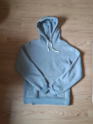  (storlek L (barn), passar XS/S eller liten M)  En Maggiore Grå hoodie med tryck på ryggen - Säljer en grå hoodie med huva och vita dragsnören. På ryggen finns ett stort svartvitt tryck med motiv och texten 'Maggiore. Hoodien har en klassisk känguruficka framtill och ribbade muddar vid ärmar och nederkant. Perfekt för en chill och avslappnad stil.