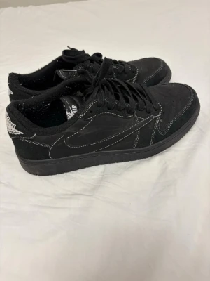Jordan 1 low black phantom - Snygga svarta Nike Air Jordan 1 Low sneakers med kontrasterande vita sömmar. Skorna har ovandel i mocka och läder, klassisk snörning och diskret logga på hälen. Perfekta för dig som gillar stilrena och sportiga sneakers.