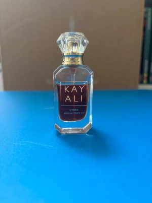 Kayali Utopia Vanilla Coco  10 ml parfym - Kayali Utopia Vanilla Coco 21 är en lyxig parfym i en elegant, genomskinlig glasflaska med gulddetaljer och kristalliknande kork. Doften har inslag av vanilj och kokos, och flaskan har en modern, stilren design med fyrkantig form. Säljer pga använder ej längre, inköpt på Sephora. Förvarats mörkt och svalt.